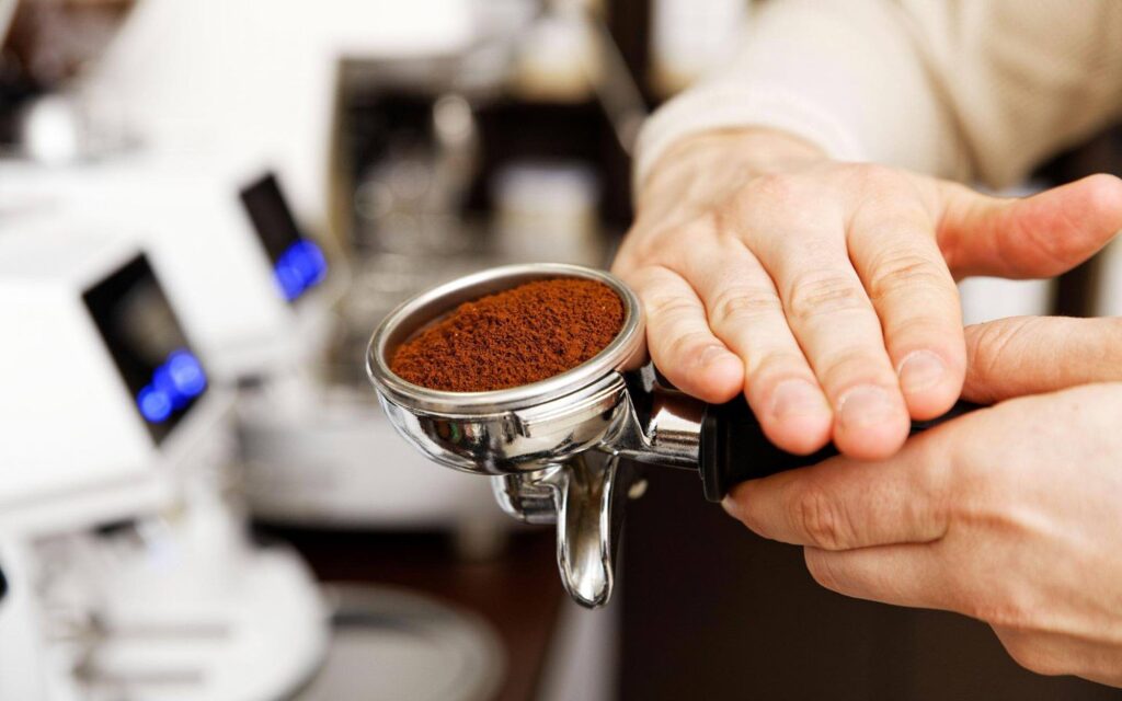 mãos de um barista segurando porta-filtro e distribuindo o café antes da extração